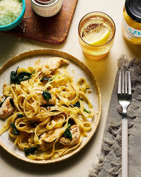 Taglietelli with Preserved Lemons, Chicken and Spinach next to a jar of Belazu preserved lemons and Épices de Cru aleppo pepper and a sprinkle of Parmesan cheese. 