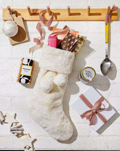 White faux-fur stocking filled with Diaspora Co chai masala, a chocolate bar and ras el hanout, beside Flavourfull shortbread and Kitten and the Bear jam