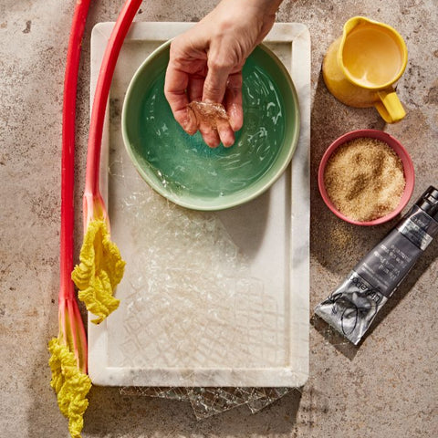 A hand soaking gelatine leaves in a bowl of water